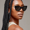 Model of color wearing oversize glossy black cateye sunglasses with silver metal detailing