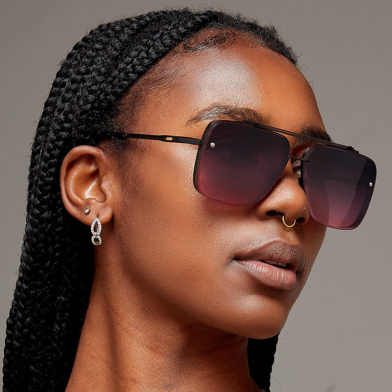Woman of color wearing faded purple to pink oversize square aviators with no nose pads.